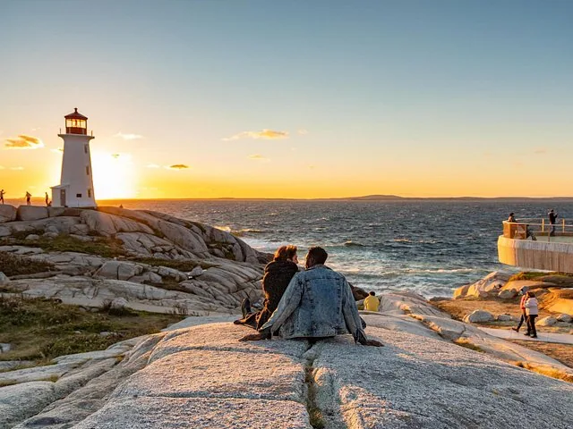 Ein Paar sitzt auf Felsen und beobachtet den Sonnenuntergang am Leuchtturm von Peggy's Cove