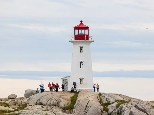 White lighthouse with a red top on rocky terrain with visitors