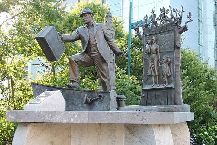 Bronze sculpture of a man carrying luggage with a family depicted nearby