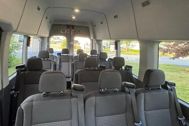 Inside a tour van looking towards the back with empty grey seats.