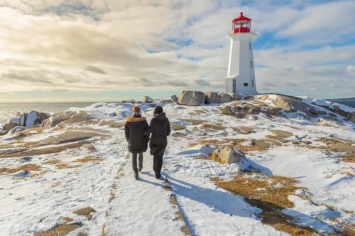 Menschen gehen über schneebedeckte Felsen auf einen weiß-roten Leuchtturm zu